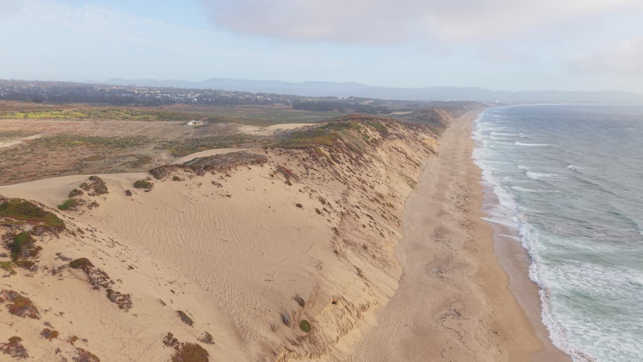 Static aerial shot in downward view over dunes, beach, and ocean at Fort Ord Dunes State Park, followed by a gentle elevation