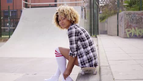 Young-woman-sitting-on-her-skateboard-at-the-rink