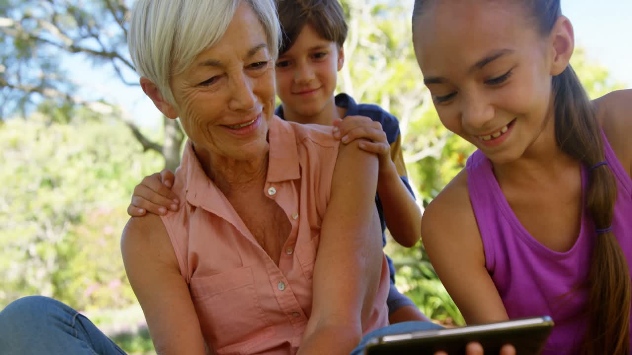 abuela y nietos usando teléfono móvil en el parque 4k