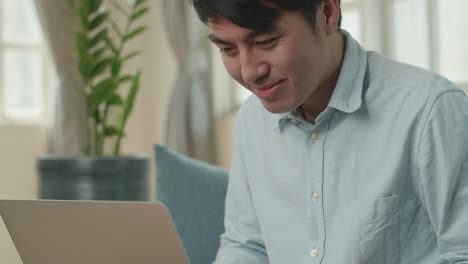 asian male working on laptop and smiling at living room, video in 4k