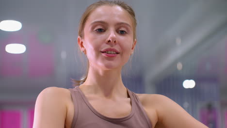 close-up of young woman working out, engaging in deep stretch exercise with soft bokeh ceiling lights, she smiles warmly, focused on flexibility and movement in a bright