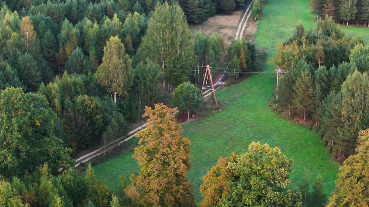 Aerial orbit of electricity pylon and narrow drit road in countryside rural region, green surroundings