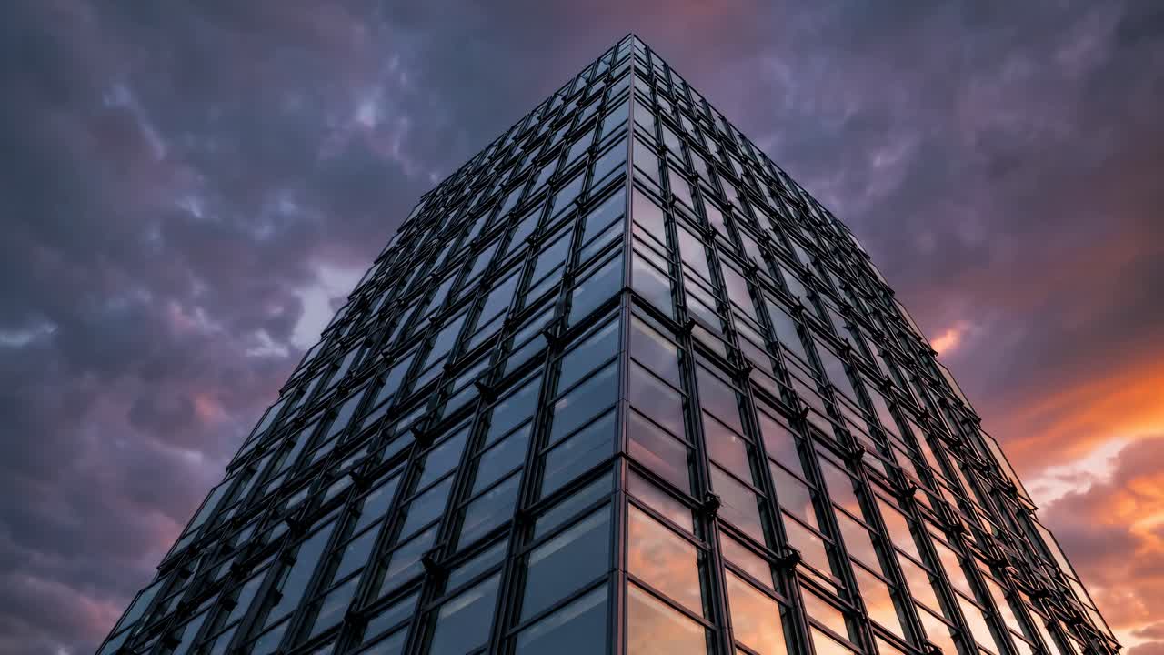 Dramatic low-angle shot of a modern glass building against a moody sky, capturing the urban