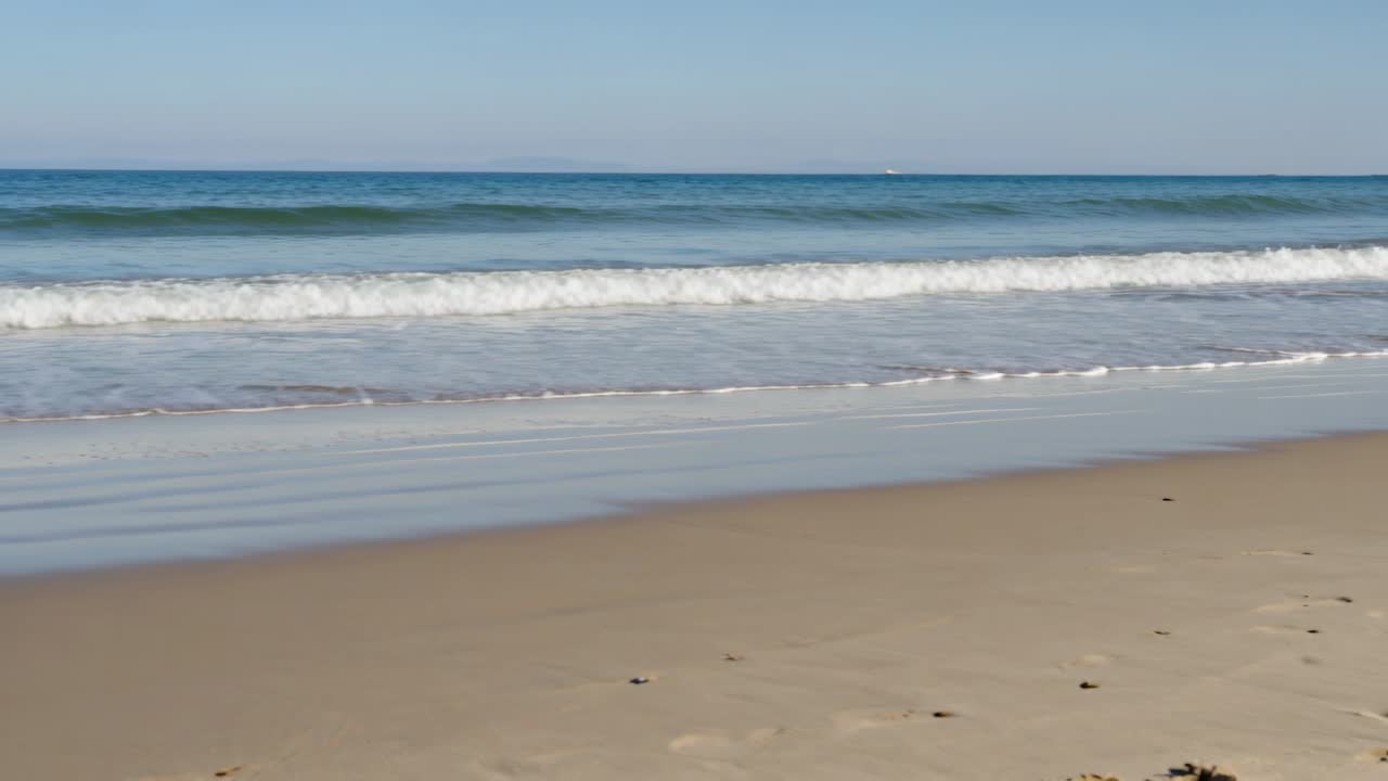 Vagues littorales en mouvement venant de l'horizon, déferlant sur la plage de sable et montrant des empreintes de pas.