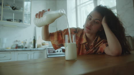 depressed woman leaning on kitchen table, pouring milk into glass