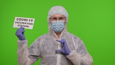 un trabajador de la salud con un traje de protección que sostiene un cartel que dice "estación de vacunación contra covid-19"