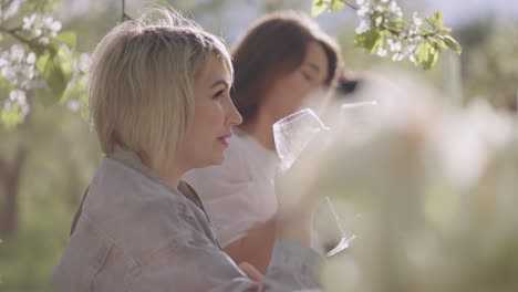 joyful women are drinking wine garden party for friends and family in blooming orchard in spring day