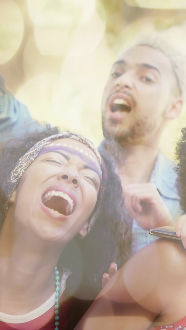 Video vertical: Dos adultos cantando y bailando en un festival de música, un teléfono filma generando alegría con efecto bokeh.
