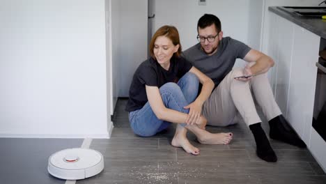 a young married couple is testing a new robot vacuum cleaner. smart home devices