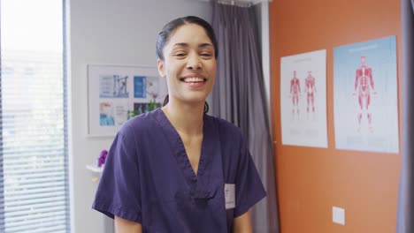 Portrait-of-happy-biracial-female-physiotherapist-smiling-in-physical-therapy-unit-at-hospital