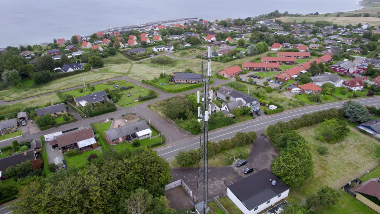 A tall cell tower rises above a peaceful Danish suburban neighborhood with houses, roads and green spaces visible from an aerial view