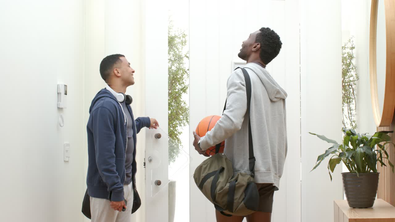 Arriving at hall, diverse male friends spinning basketball while opening door letting light inside