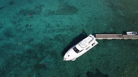 people swimming in crystal clear water of blue lagoon in veliki budikovac with a ferretti yacht moored to wooden jetty