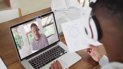 African-american-male-college-student-holding-notes-while-having-a-video-call-on-laptop-at-home