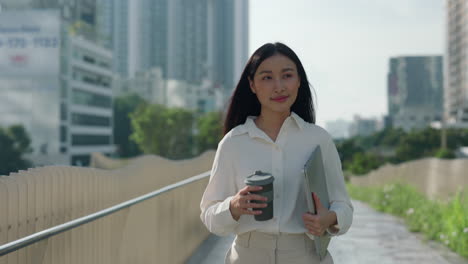 young woman walking in the city with a laptop and coffee