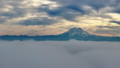 white fluffy clouds revealing mount rainier on sunset horizon in washington state, usa