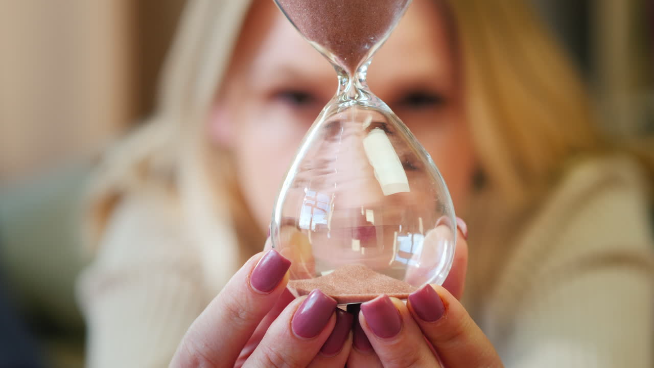 A woman looks at an hourglass