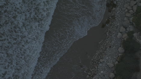 top down view of ocean waves crashing against an rocky sand beach from above