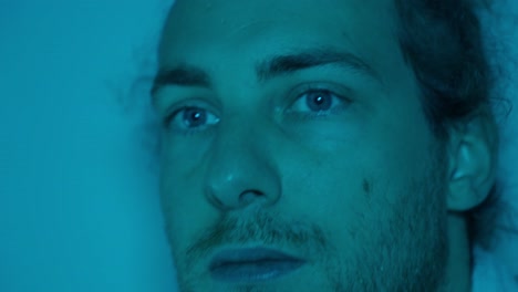 side profile of man in blue light, quiet expression turning to look forward at angle, atmospheric soft shadows across face