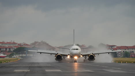 airplane approaches runway, creating water spray on landing, with cloudy sky and urban background enhancing the scene
