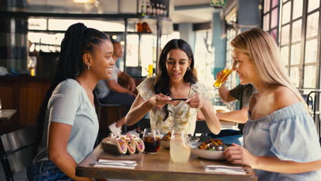 group of female friends meeting up in restaurant taking photo of food on mobile phone