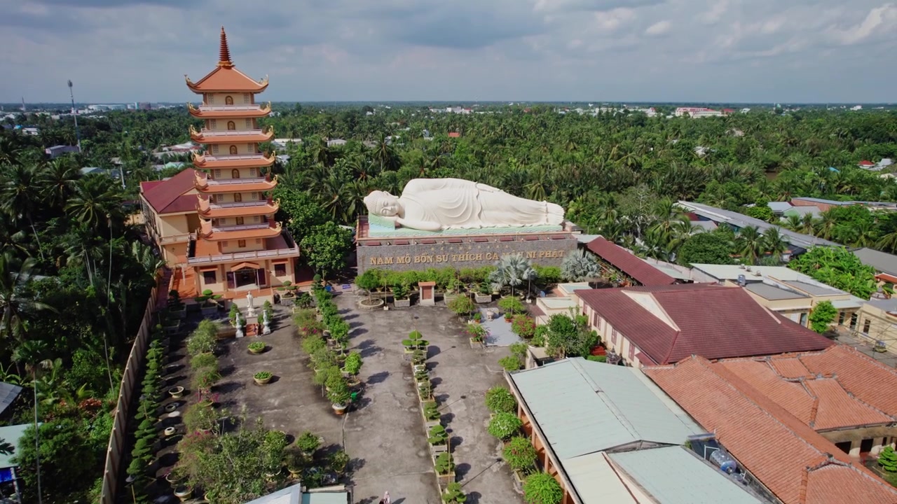 Plano aéreo cinematográfico sobre o complexo do templo budista Vinh Trang em My Tho, apresentando seu famoso Buda Reclinado, torre de pagode e esculturas religiosas monumentais