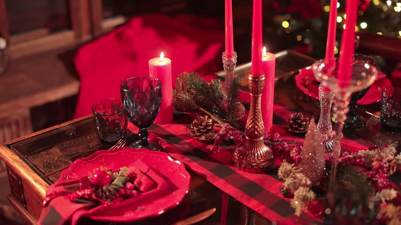 Beautifully decorated table for Christmas celebration. Luxurious plates, glasses and candlesticks, pine branches, cones and berries in red colors.