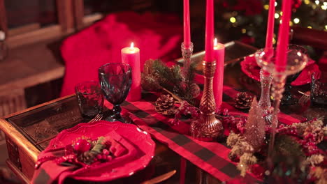 beautifully decorated table for christmas celebration. luxurious plates, glasses and candlesticks, pine branches, cones and berries in red colors.