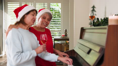 senior women celebrating christmas, playing piano and enjoying wine at home