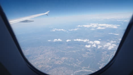 aerial view from airplane window showing clouds and land during day flight