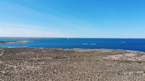 Aerial view of a barren landscape with a cruise ship in the distant sea, under clear skies