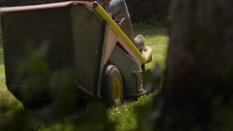 gardener driving lawn mower around garden on sunny day