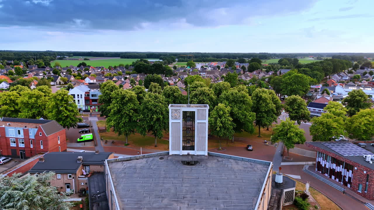Approaching the belfry with three bells on the church. Picturesque residential area around. The Netherlands. Aerial view