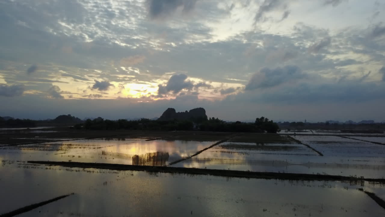 n amazing view of sunset reflecting in a flooded agricultural area in Ninh Binh, Vietnam, on a cloudy day. The still water creates a mirror image of the dramatic sky and landscape.