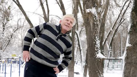 an elderly european man does a morning outdoor warm-up in the winter, exercise for the lower back, leanings forward. healthy life concept. 60 fps