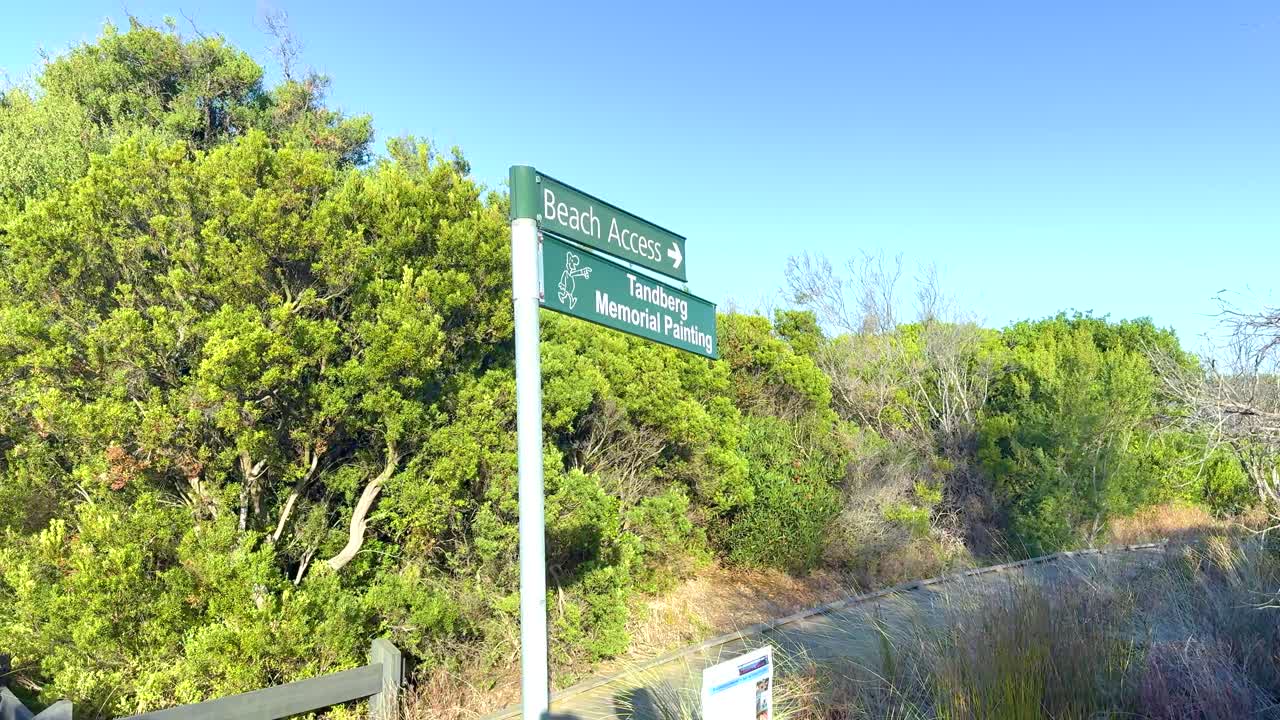 A green signpost marks a coastal pathway surrounded by lush vegetation under clear blue skies in Queenscliff, Victoria