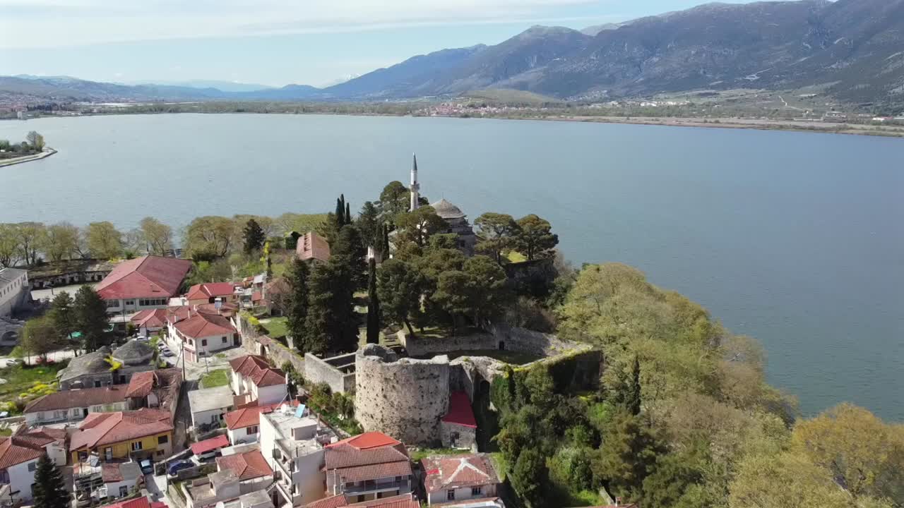Telecamera drone che vola dritta verso la storica Moschea di Aslan Pasha sul fianco della scogliera del Castello di Ioannina in Grecia, con lo scenografico Lago Pamvotida e le montagne sullo sfondo