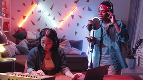 asian woman and black rapper recording music in home studio
