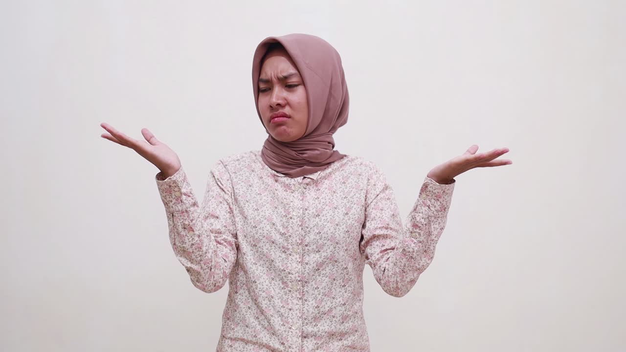 Confused young asian muslim girl standing between two choice and showing puzzled face expression gesture
