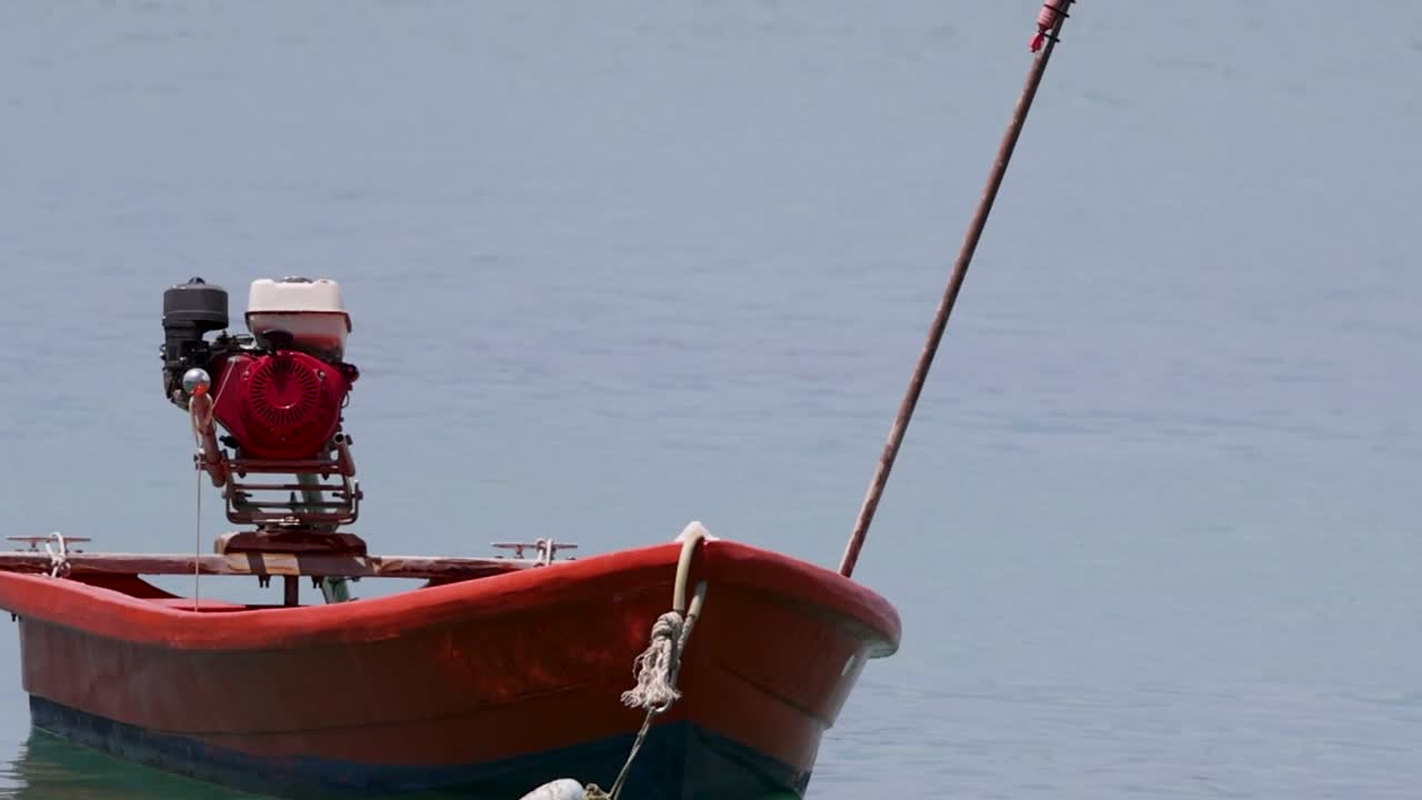 A red boat with an engine is moored on calm waters, showcasing a peaceful maritime scene.