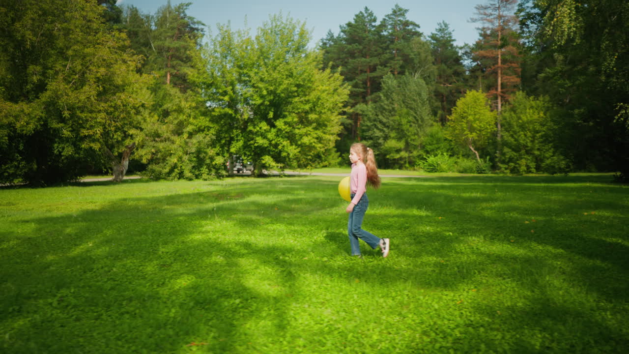 Side view of young girl walking joyfully with yellow balloon under arm across lush grassy field surrounded by trees on bright day with car seen passing in distant background near forested road