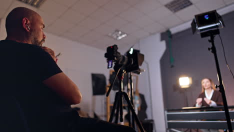 cameraman looks at his camera attentively. low angle view. female blogger talks sitting at desk opposite to the photographer. blurred backdrop.
