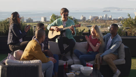 Un-Joven-Caucásico-Tocando-La-Guitarra-En-Una-Azotea-Con-Sus-Amigos.