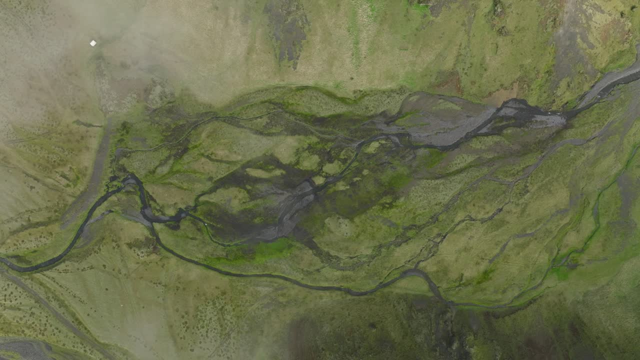 A striking aerial view of a braided river system winding through the landscape of Hafursey, Iceland, showcasing intricate water channels and lush greenery.