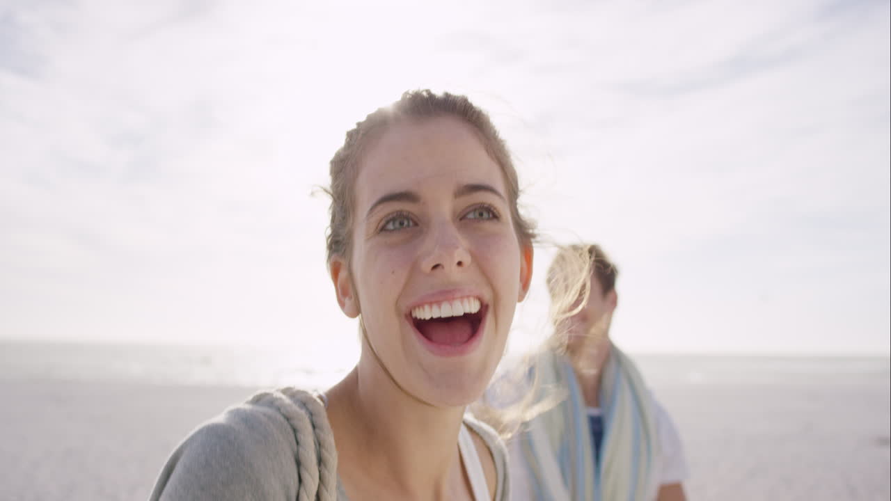 Giovane coppia che si tiene per mano, la donna che guida il fidanzato mentre camminano verso il tramonto su una spiaggia deserta godendosi la natura