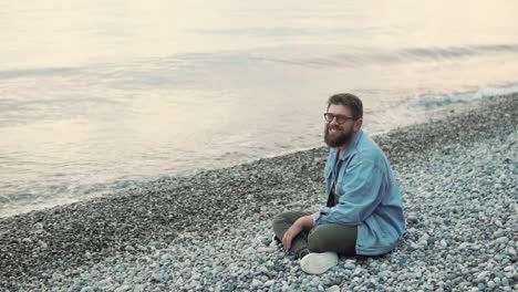 man sitting on a pebble beach at sunset