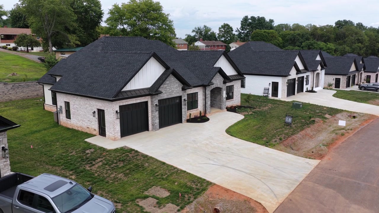 Uma casa recém-acabada de pedra e tijolo branco com um telhado de duas águas íngreme e escuro e garagem tripla fica em gramado fresco em um empreendimento em Lynchburg, Virgínia. Imagem aérea de aproximação.