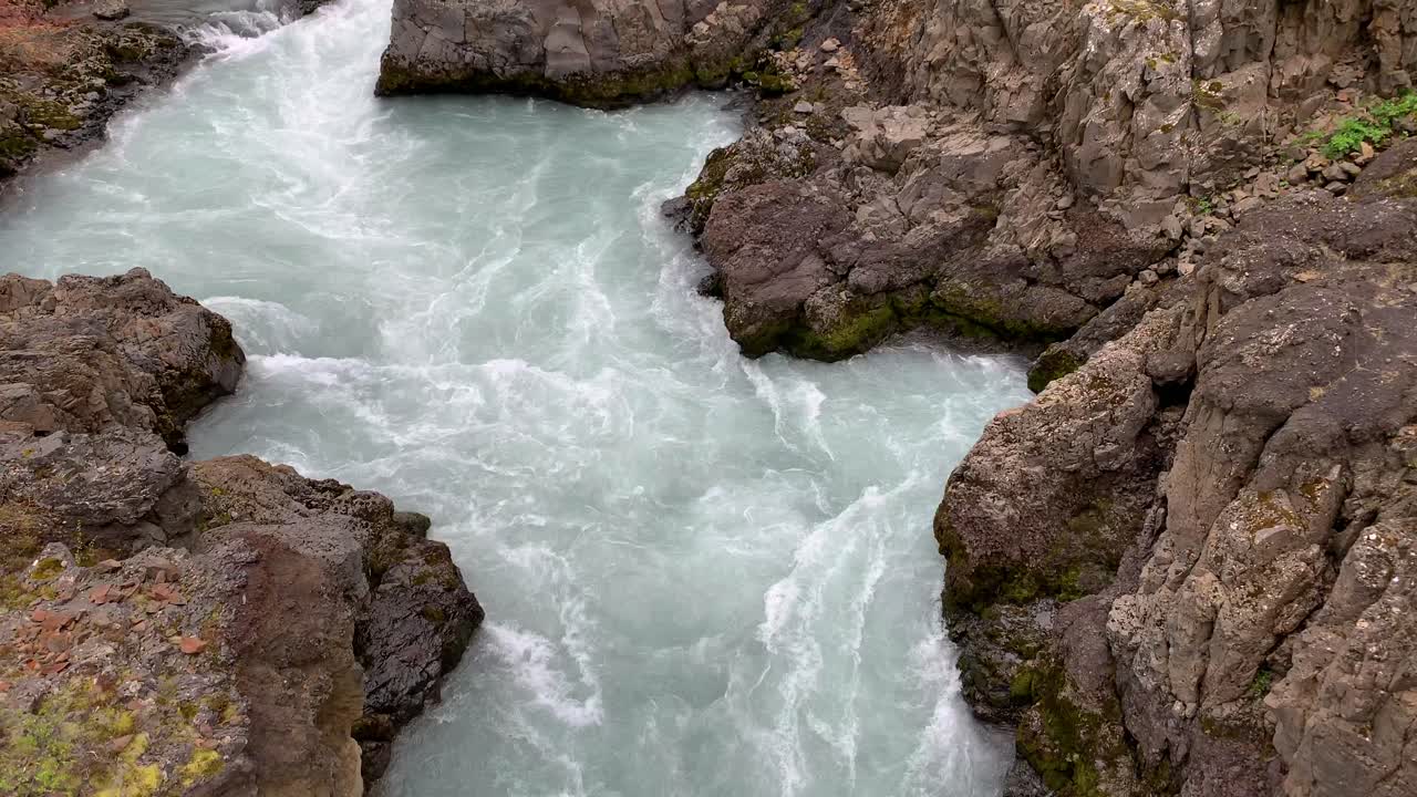 The lightblue water of the gorgeous waterfall Barnafossar flowing around the rocks that surround the water