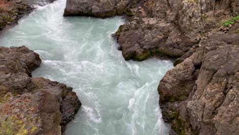 the lightblue water of the gorgeous waterfall barnafossar flowing around the rocks that surround the water
