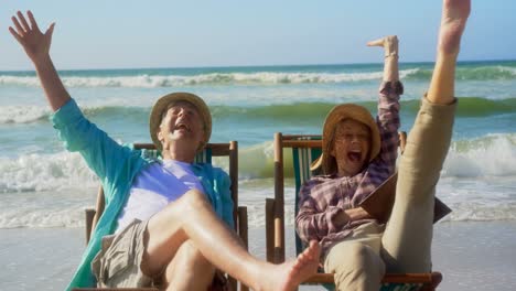 front view of active senior caucasian couple having fun on a sun lounger at beach 4k